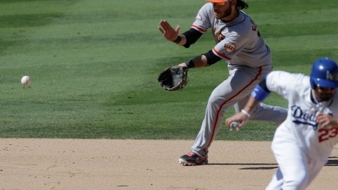 Brandon Crawford, paracorto de los Gigantes, fildea un roletazo mientras Adrián González (der.) se repliega a la segunda base.