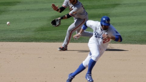 Brandon Crawford, paracorto de los Gigantes, fildea un roletazo mientras Adrián González (der.) se repliega a la segunda base.