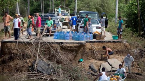 Personas esperan al borde de un puente destruído, para transportar en embarcaciones la ayuda a damnificados.
