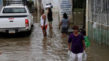Un grupo de personas carga provisiones en una zona inundada, en una colonia del puerto de Acapulco (México), ayer.