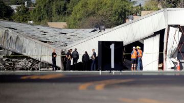 Autoridades del aeropuerto e investigadores frente al hangar que se derrumbó al estrellar una avioneta en el aeropuerto de Santa Monica el domingo por la noche. Los investigadores esperaban la llegada de una grúa el lunes para poder llegar al avión, enterrado por el derrumbe.
