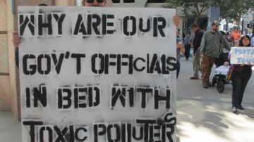 Manifestante  con una pancarta  que dice: ¿Por qué los  funcionarios del estado  están en la cama con contaminadores?