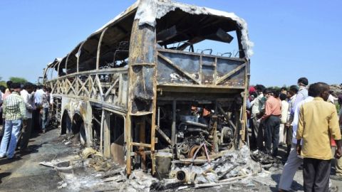 Una multitud de gente se concentra en el lugar donde un autobús se ha incendiado, después de chocar contra una barrera vial, en India.