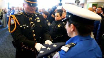 El oficial de policía de LAX Tom Dye pasa a la Bandera de Honor de EEUU a la  guardia de honor Brandy Richards, de TSA, en el Aeropuerto Internacional de Los Ángeles, en un acto en memoria de del agente de TSA Gerardo Hernández.