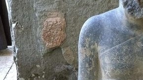 Estatua de un sacerdote de alto rango arrodillado y con vestimenta religiosa frente a una mesa de ofrendas.