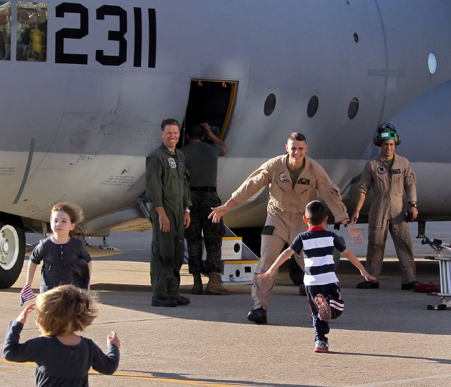 Niños scorren hacia un C-130 a recibir asus papás, marines de EEUU que regresan a casa después de cumplir misiones en el ultramar.