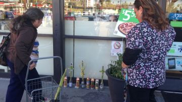 Amigos del fallecido ponen flores en un altar que se colocó frente a la tienda en donde trabajaba.