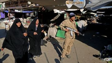 Un efectivo de seguridad hace guardia mientras que mujeres caminan por el lugar de un atentado en una sección cristiana de Bagdad, Irak el miércoles, 25 de diciembre 2013.