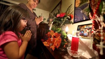 Irma Plascencia y su hija Mia, de 4 años, rezan junto al altar del padre, Israel Plascencia, en su casa de Pomona.