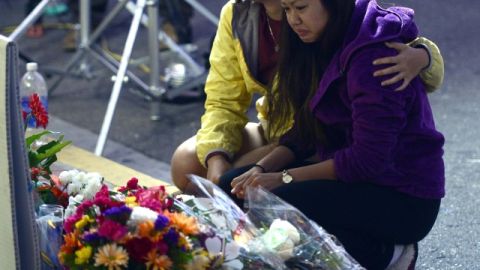 Dos jóvenes arrodilladas luego de colocar flores ante un altar que se levantó cerca al deli donde murió una de las víctimas del asesinato masivo del sábado.