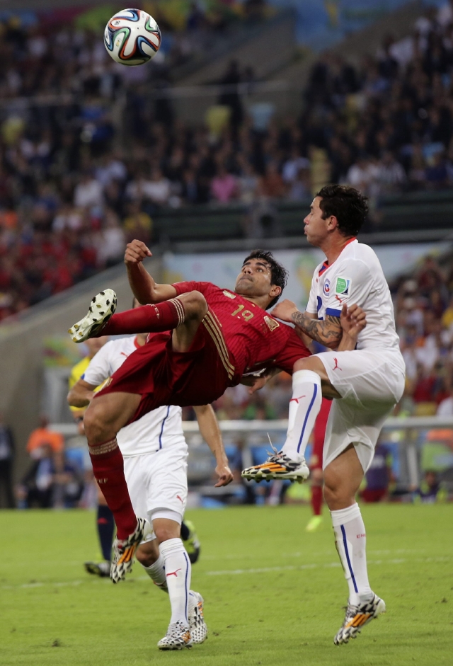 El delantero de la selección de España,  Diego Costa, trata de rematar tendido en el aire ante la mirada de los chilenos  Eugenio Mena  y Arturo Vidal.