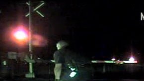 Cámaras en la patrulla muestran cuando  el agente Morales sale corriendo de la patrulla, se acerca a la fémina, y la arrastra por el suelo hasta moverla a espacio seguro.