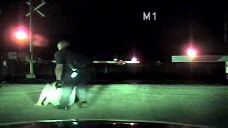 Cámaras en la patrulla muestran cuando  el agente Morales sale corriendo de la patrulla, se acerca a la fémina, y la arrastra por el suelo hasta moverla a espacio seguro.