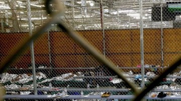 Dos niñas ven televisión delante de varios menores que duermen sobre unas colchonetas en un centro de procesamiento de Arizona.