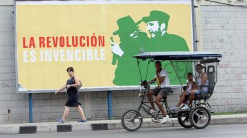 Varias personas pasan frente a una valla alusiva al nuevo aniversario de la Revolución cubana.