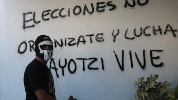 Un hombre encapuchado hace una pintada en una pared, durante una nueva jornada de protestas en rechazo a la desaparición de 43 estudiantes en  Iguala.