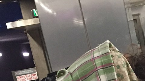 Una anciana con una bata de hospital, descansa en la estación de Metro de Vermont y Santa Monica en Los Ángeles.
