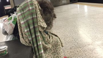 Una anciana con una bata de hospital, descansa en la estación de Metro de Vermont y Santa Monica en Los Ángeles.