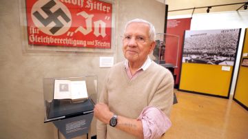 Robert Clary, un sobreviviente del holocausto, posa junto a un afiche Nazi que es parte de la exhibición en la biblioteca. / (Foto: Aurelia Ventura/La Opinion)