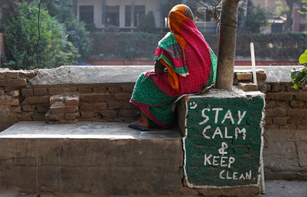 Una mujer nepalesa descansa sentada junto a una pintada con el mensaje "Permanece tranquilo y limpio" mientras siguen las obras de reconstrucción de un grifo de agua potable comunitario que resultó dañado en el terremoto, en Katmandú, Nepal.