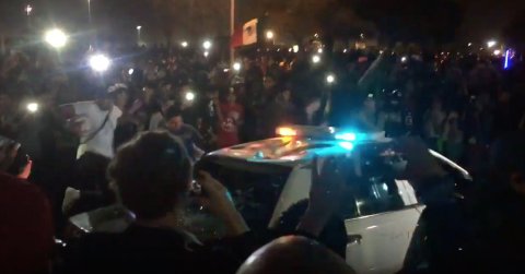 Manifestantes rodearon una patrulla y empezaron a romper las ventanas y saltar sobre el auto.