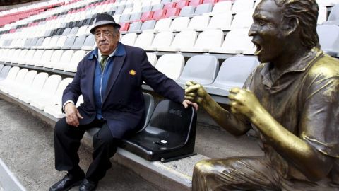 Melquiades Sánchez Orozco, la voz oficial del Estadio Azteca, posa con "Nachito", estatua localizada en uno de los asientos como monumento a los aficionados.