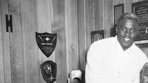 Jackie Robinson aparece en esta foto de 1956 mostrando algunos de sus trofeos en su casa de Brooklyn. Artefactos históricos suyos y de otras leyendas de los Dodgers serán exhibidos en Dodger Stadium.