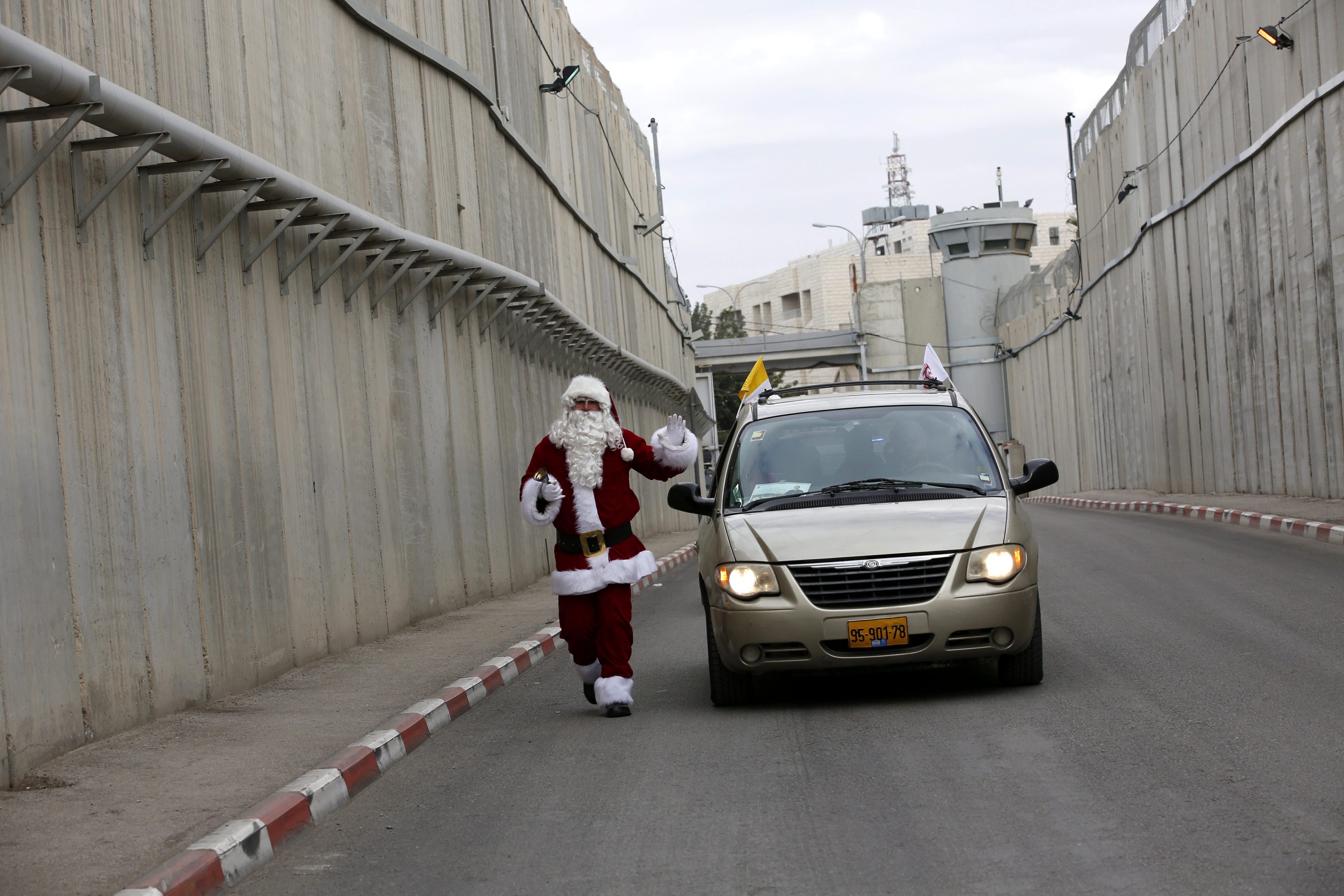 Un palestino vestido de Santa Claus saluda al Patriarca latino de Jerusalén que llega a través de un puesto de control israelí para asistir a las celebraciones de Navidad, en la ciudad cisjordana de Belén, el 24 de diciembre de 2016. EFE
