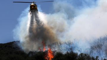 Un helicóptero de extinción de incendios vuela sobre colinas ardientes en Thousand Oaks.