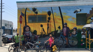 Miembros de TRUST South LA frente a un mural celebrando andar en bicicleta.