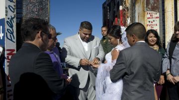 Brian Houston le pone un anillo a su prometida Evelia Reyes durante la celebración de su boda en una de las puertas de la valla fronteriza.