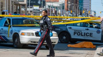 Vista de un cuerpo cubierto (d) después de que una camioneta alquilada recorriera la acera golpeando a los peatones hoy, lunes 23 de abril de 2018, en la calle Yonge en el norte de Toronto (Canadá).