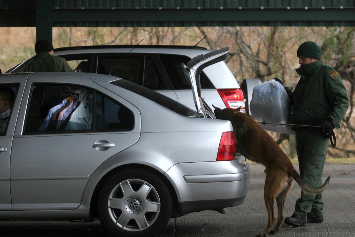 Agente de la Patrulla Fronteriza de EEUU revisa un auto con la ayuda de un perro rastreador