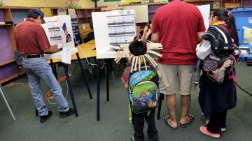 Con sus mochilas bien puestas, dos niños acompañan a su padre a votar.