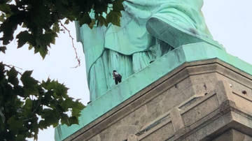 Una mujer intenta escalar la Estatua de la Libertad.