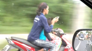 Una mujer conduce sin casco, mientras manda un mensaje de texto.