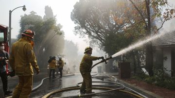 Un bombero rocía agua sobre una casa en llamas en Bel-Air durante el incendio Skirball el 6 de diciembre de 2017.