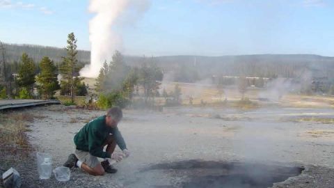 Un científico toma muestras en Ear Spring. Old Faithful se ve detrás.