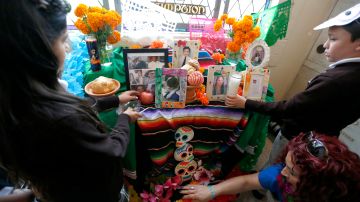 Niños colocan ofrendas en un altar del Día de Muertos. (Aurelia Ventura/La Opinion)