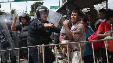 Un policía mexicano protege a un inmigrante y a su hijo durante un enfrentamiento.