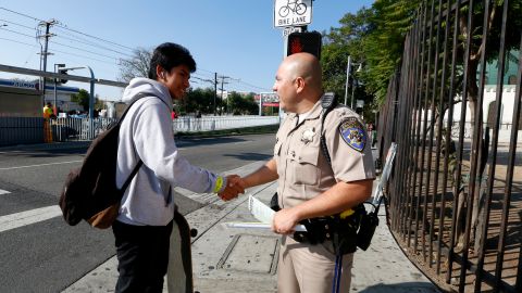 El agente J. Barrios de la Patrulla de Carreteras de California (CHP) regala una banda reflectiva a Moises Fernández en la esquina de la Avenida Vermont y el Bulevar (Aurelia Ventura/La Opinion)