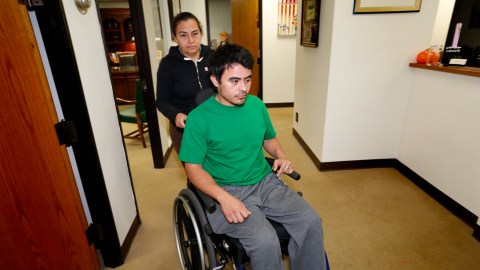 Maritza Márquez empuja la silla de ruedas de Osmin Francisco Pereira en las oficinas del abogado Alex Gálvez. (Aurelia Ventura/ La Opinion)