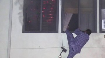 Imagen de video donde se observa a Maco Hernández colgando de la ventana de su apartamento antes de saltar y escaper de las llamas. (@KTLA)