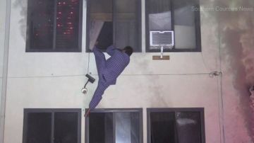 Imagen de video donde se observa a Maco Hernández colgando de la ventana de su apartamento antes de saltar y escaper de las llamas. (@KTLA)