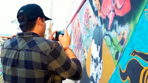 Esta imagen tomada de un video del sitio web latinx2.com muesta a un hobre fotografiando a un mural de arte hispano.