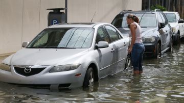 Una mujer intenta acceder a su vehículo en Miami Beach en medio de una calle inundada por el aumento del nivel del mar.