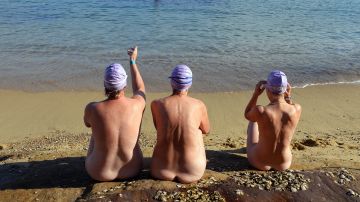 Tres mujeres sentadas en una orilla de una playa nudista de Australia.
