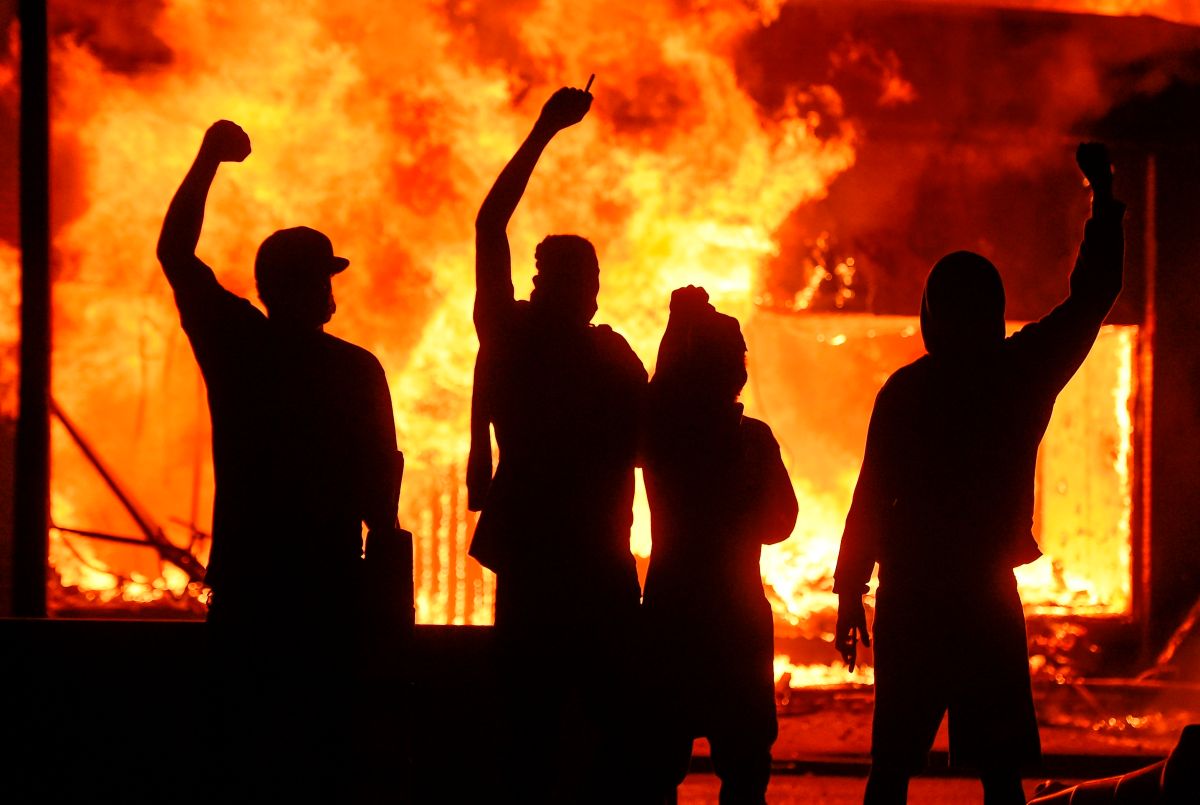 Manifestantes alzan el puño junto a una tienda en llamas en Minneapolis.