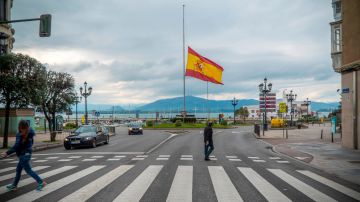 Varios peatones cruzan una calle delante de una bandera que ondea a media asta en memoria de las víctimas de coronavirus en Santander. EFE/Román G. Aguilera/Archivo