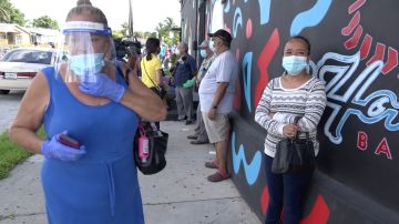 Una mujer, con máscara y guantes, esperando en fila para un entrega de mascarillas en Miami.